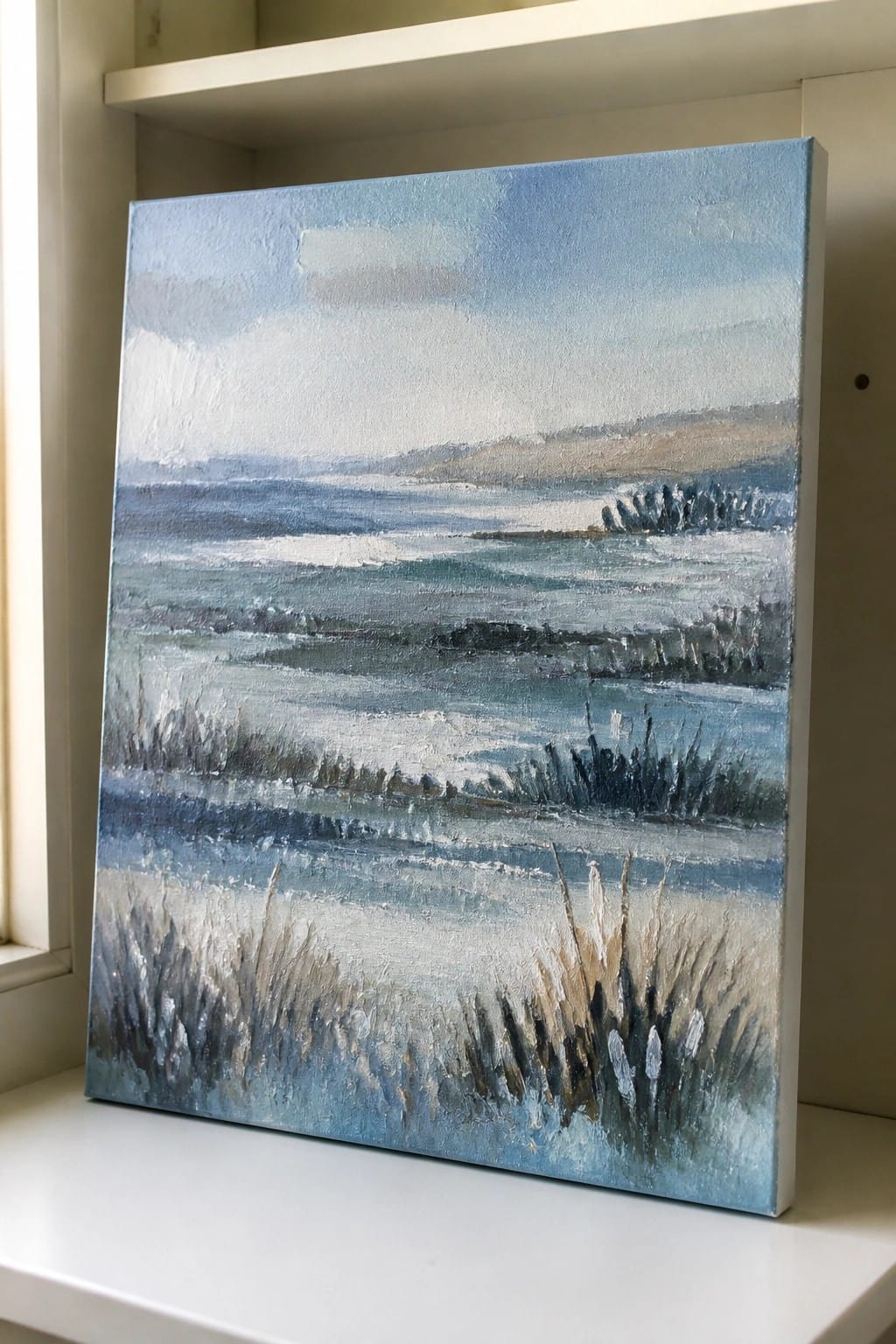 Impressionistic blue seascape painting with waves and grasses on a white shelf.