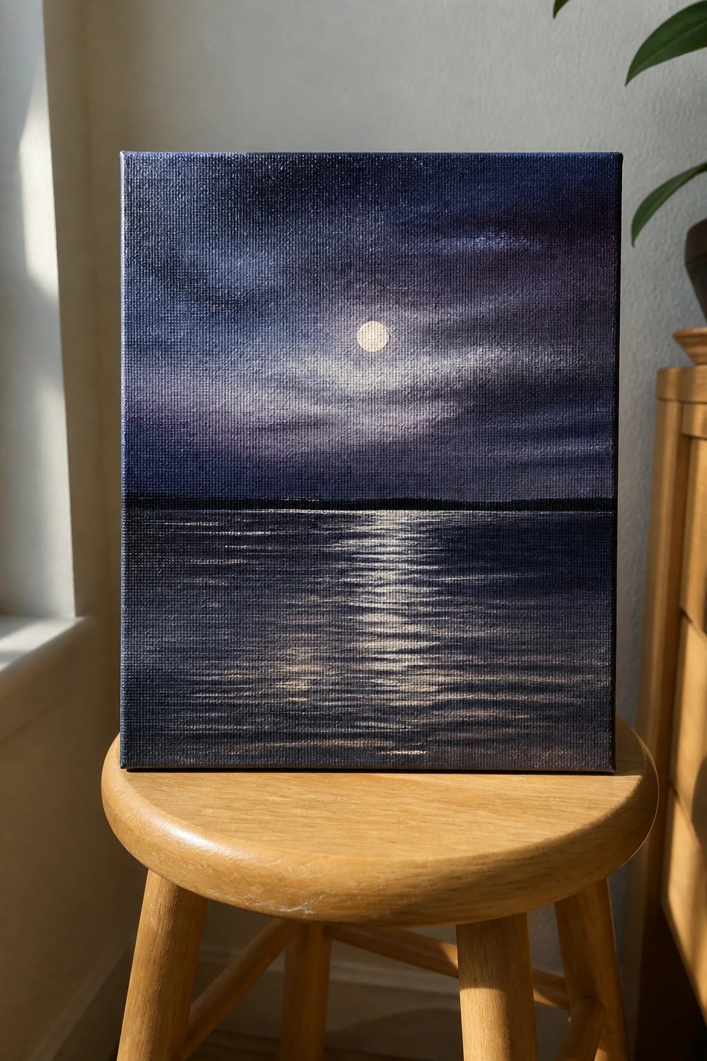 Painting of moon over dark blue sea on canvas atop wooden stool