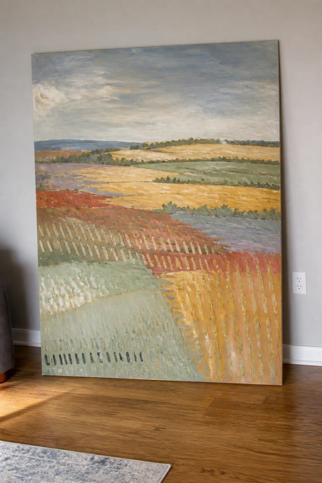 Large landscape painting of colorful fields leaning against wall on wooden floor