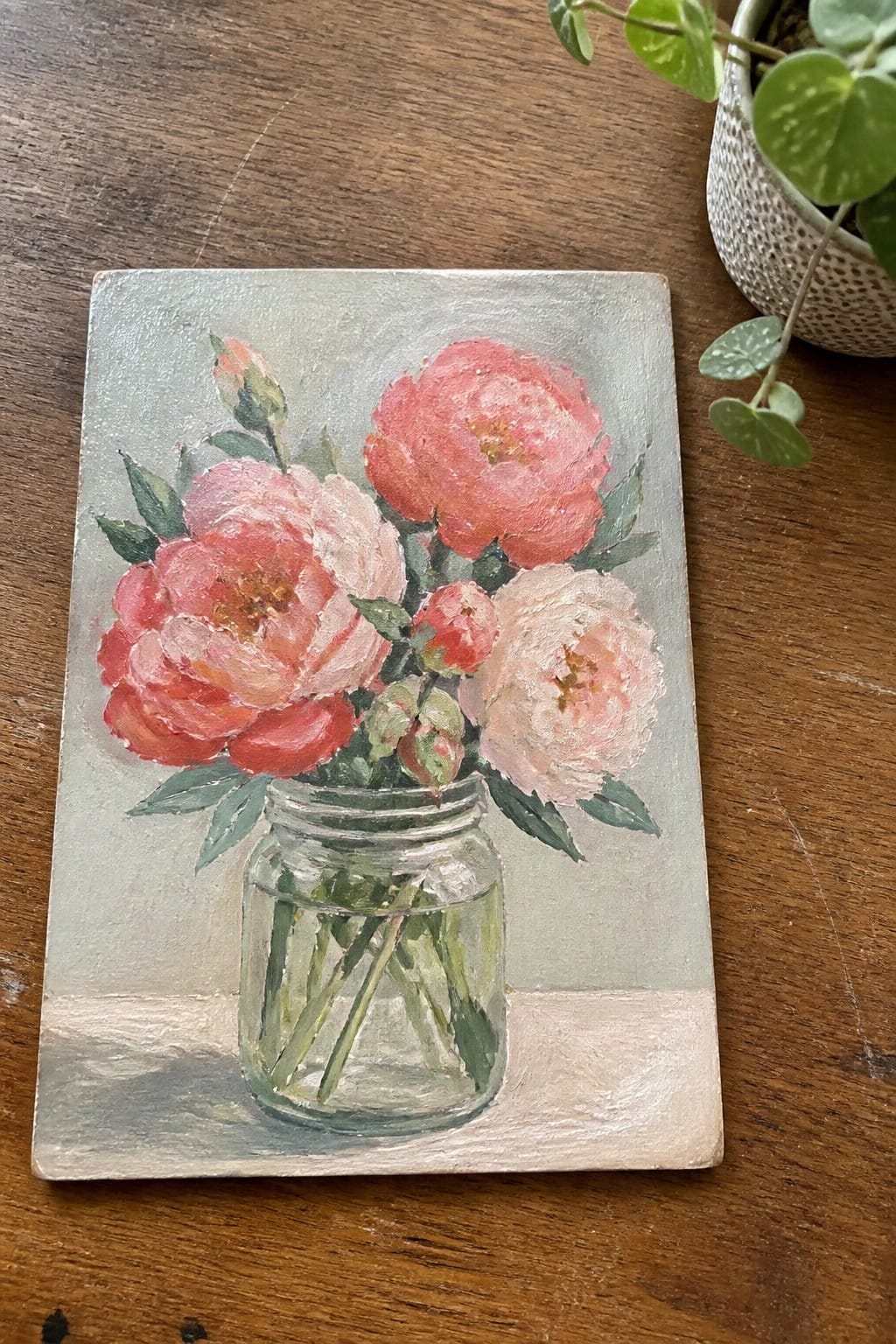 Painting of coral pink peonies in a glass mason jar on wood.