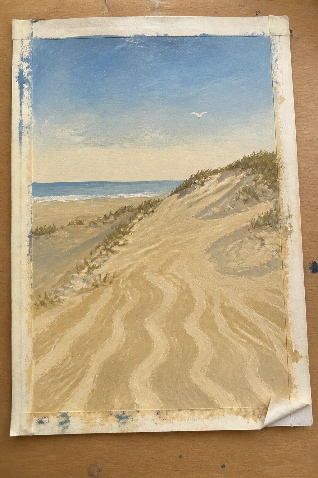 Winding sandy dunes path to ocean under blue sky with flying bird.