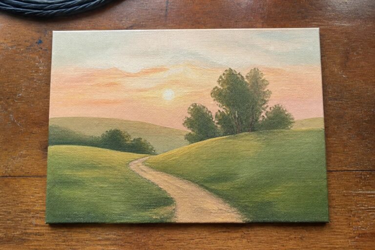 Winding dirt path curves through green meadows toward hills at pink-orange sunset.