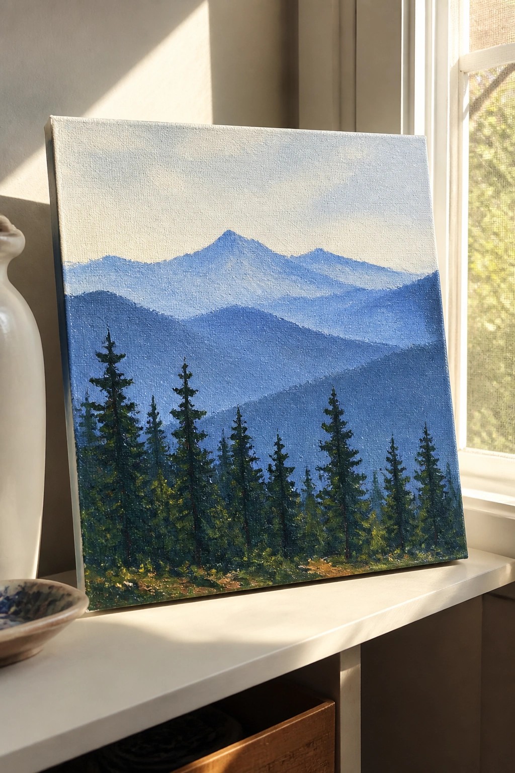 Blue mountain landscape painting with pine trees on sunny white windowsill.