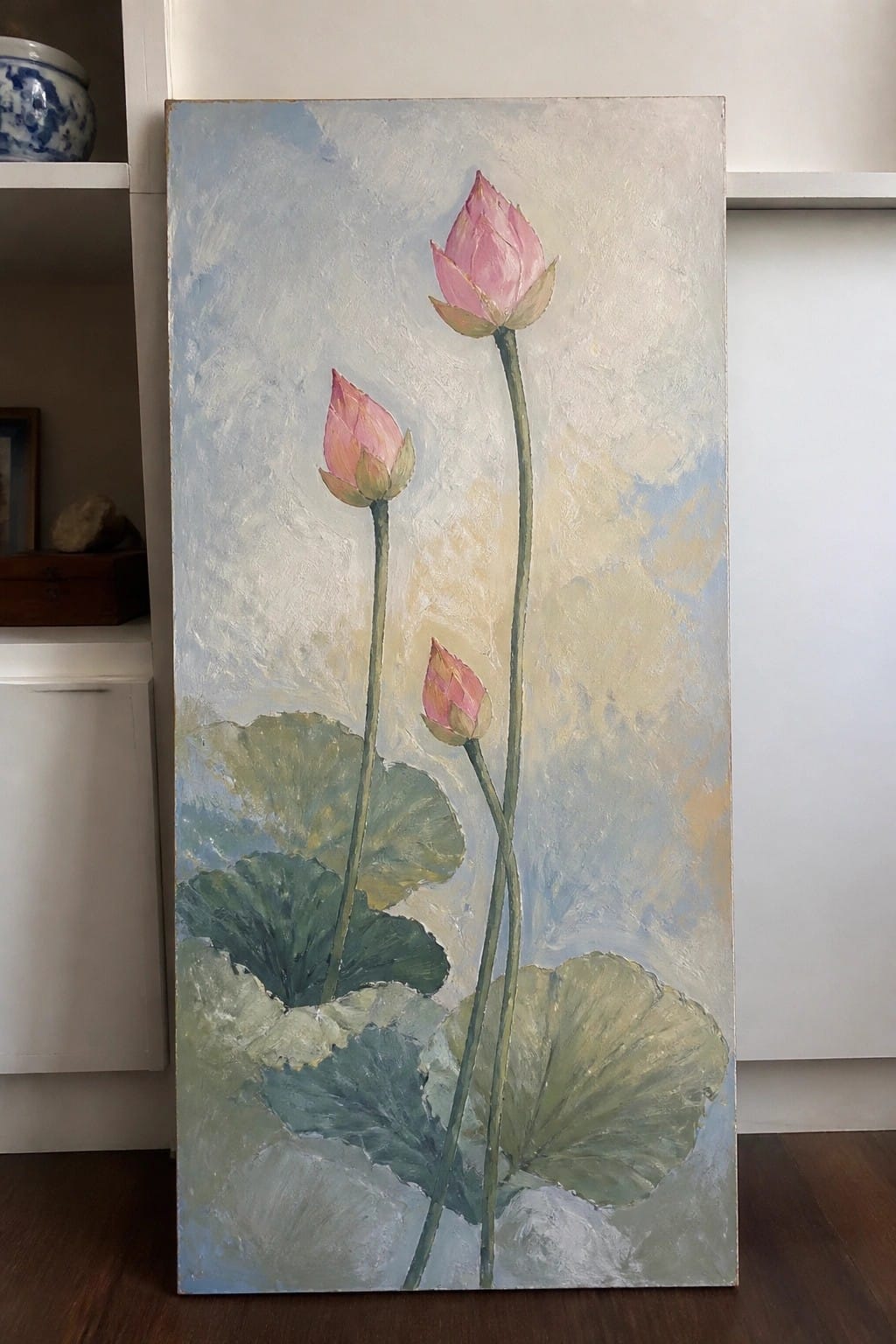 Three pink lotus buds on green stems with large leaves against a soft blue background