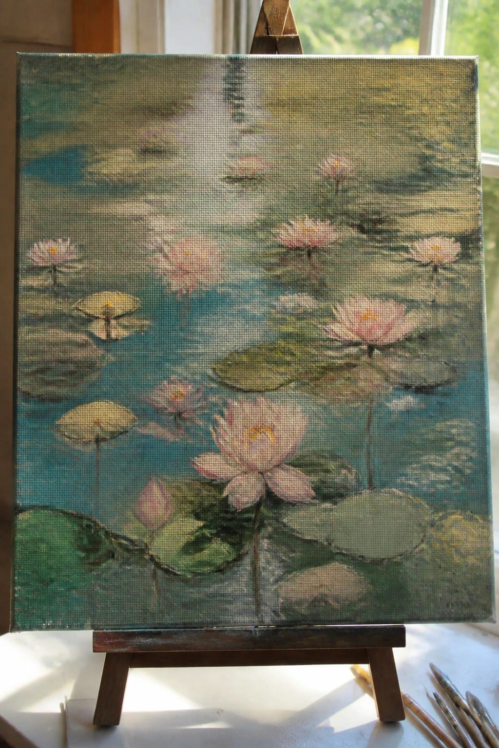 Impressionistic painting of pink water lilies on green lily pads atop wooden easel