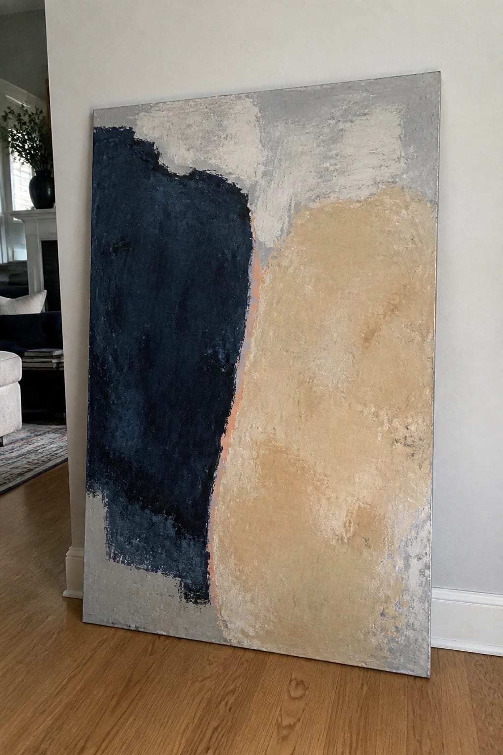A large abstract oil painting with a dark blue section on the left, a beige section on the right, and gray areas at the top and bottom, leaning against a wall.