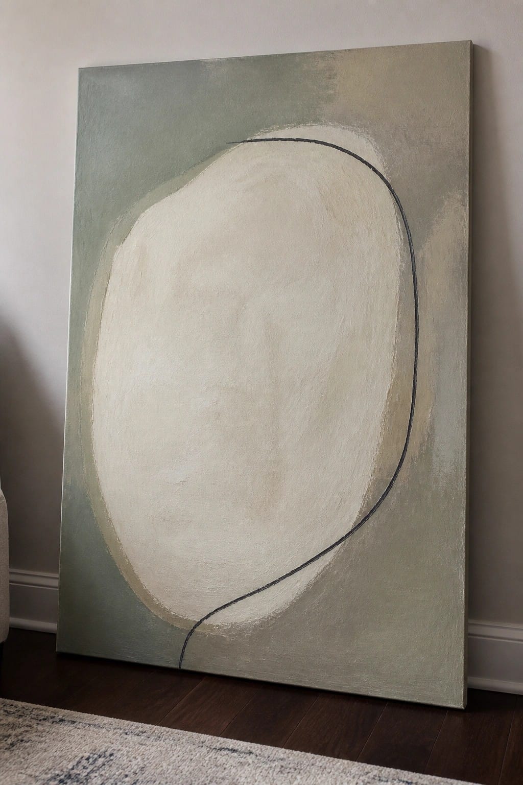Large abstract painting with beige oval and black curve on muted green, leaning on wall