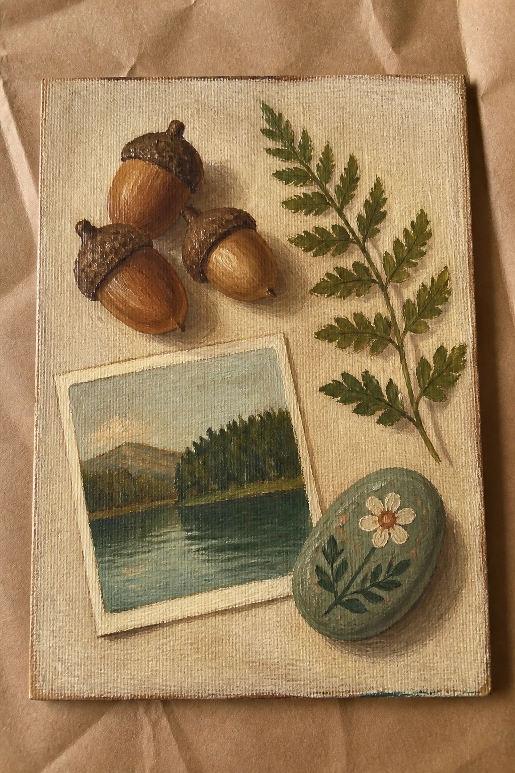 An oil painting showing three acorns, a green fern branch, a painted stone with a flower, and a small landscape of a lake and trees arranged on a canvas.