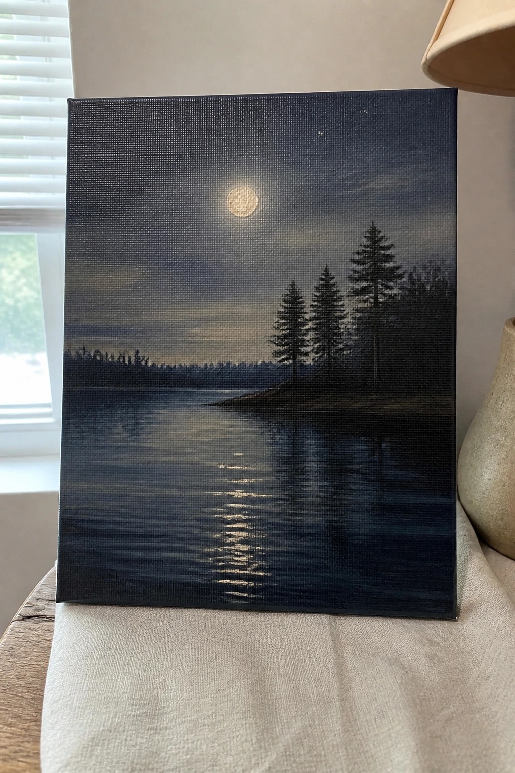 Oil painting of moonlit lake with pine tree silhouettes and glowing moon reflection.