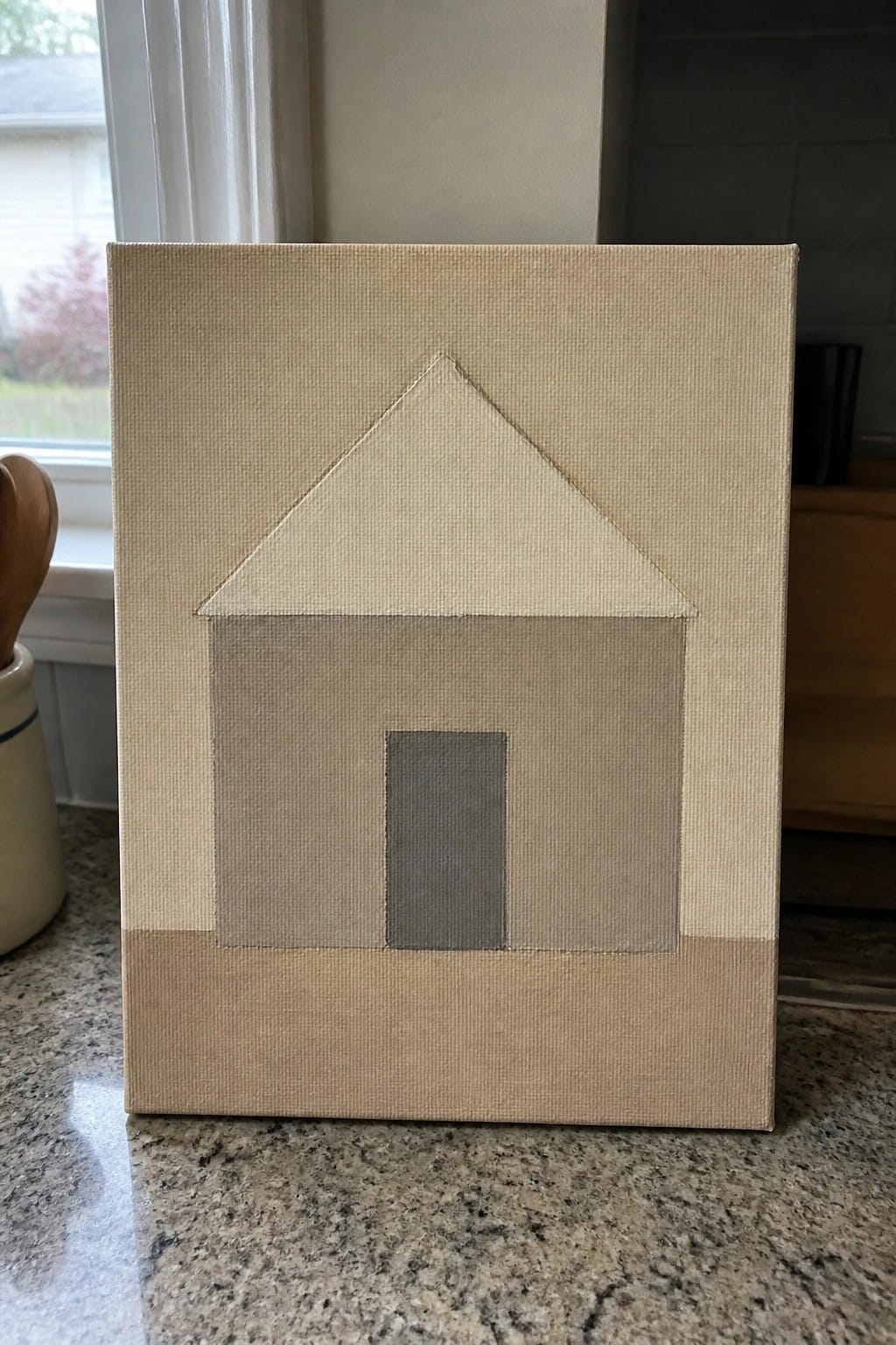 Minimalist beige canvas painting of a house with gray door on granite counter