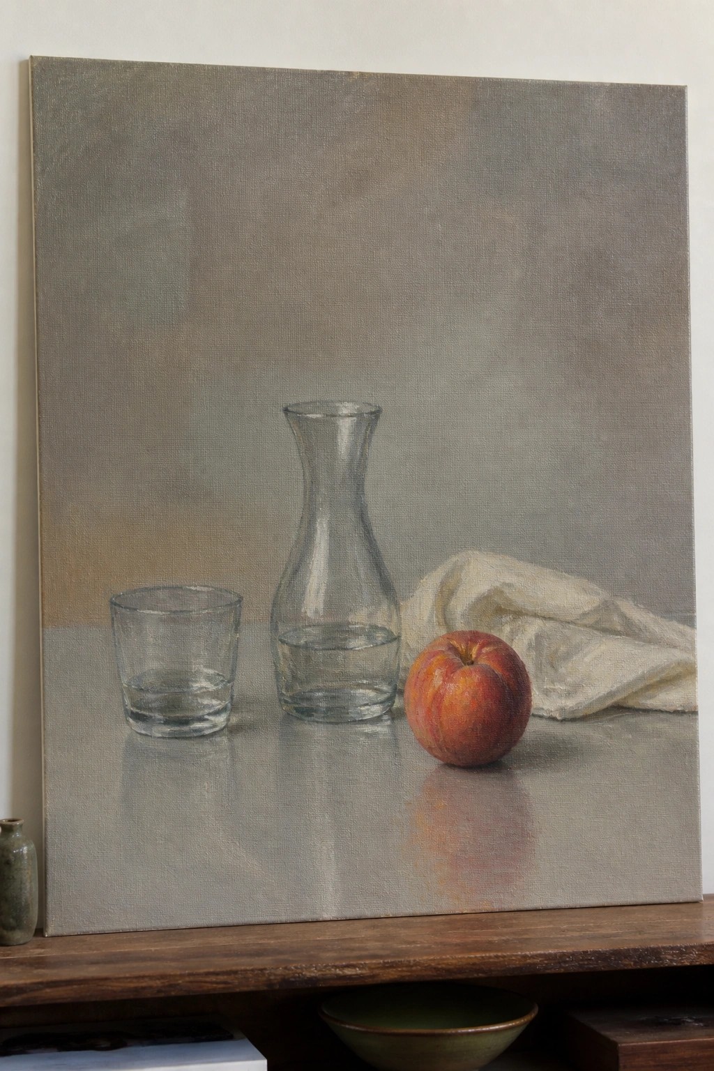 Still life with glass carafe, water tumbler, red apple, and white cloth on gray surface.