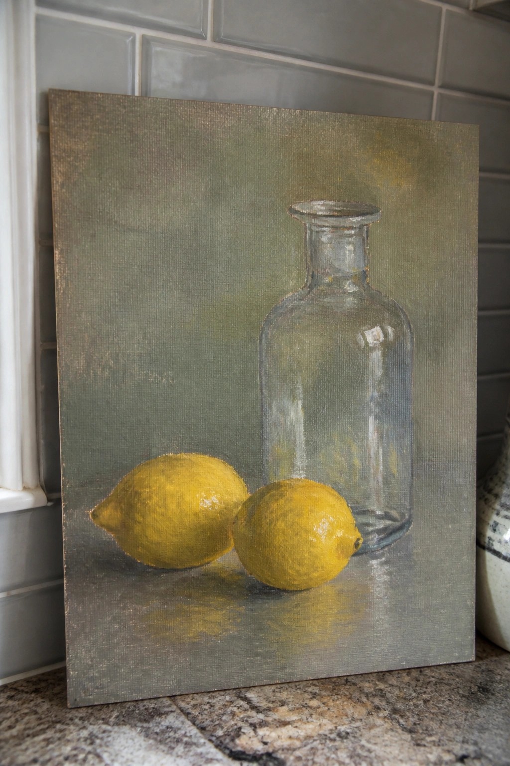 Two yellow lemons beside a glass bottle in a muted green still life painting