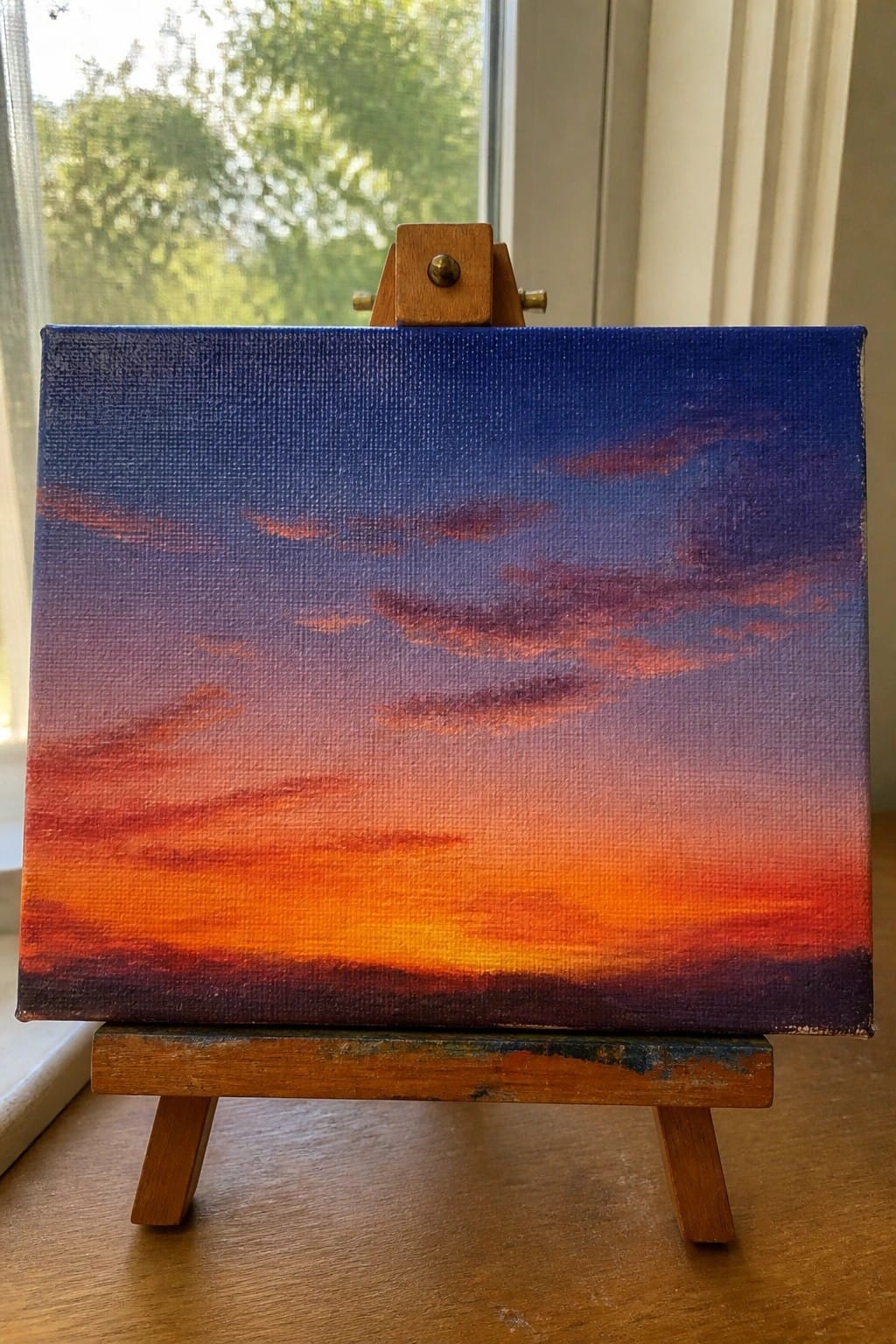 Small canvas sunset painting with blue-to-orange gradient on wooden easel.
