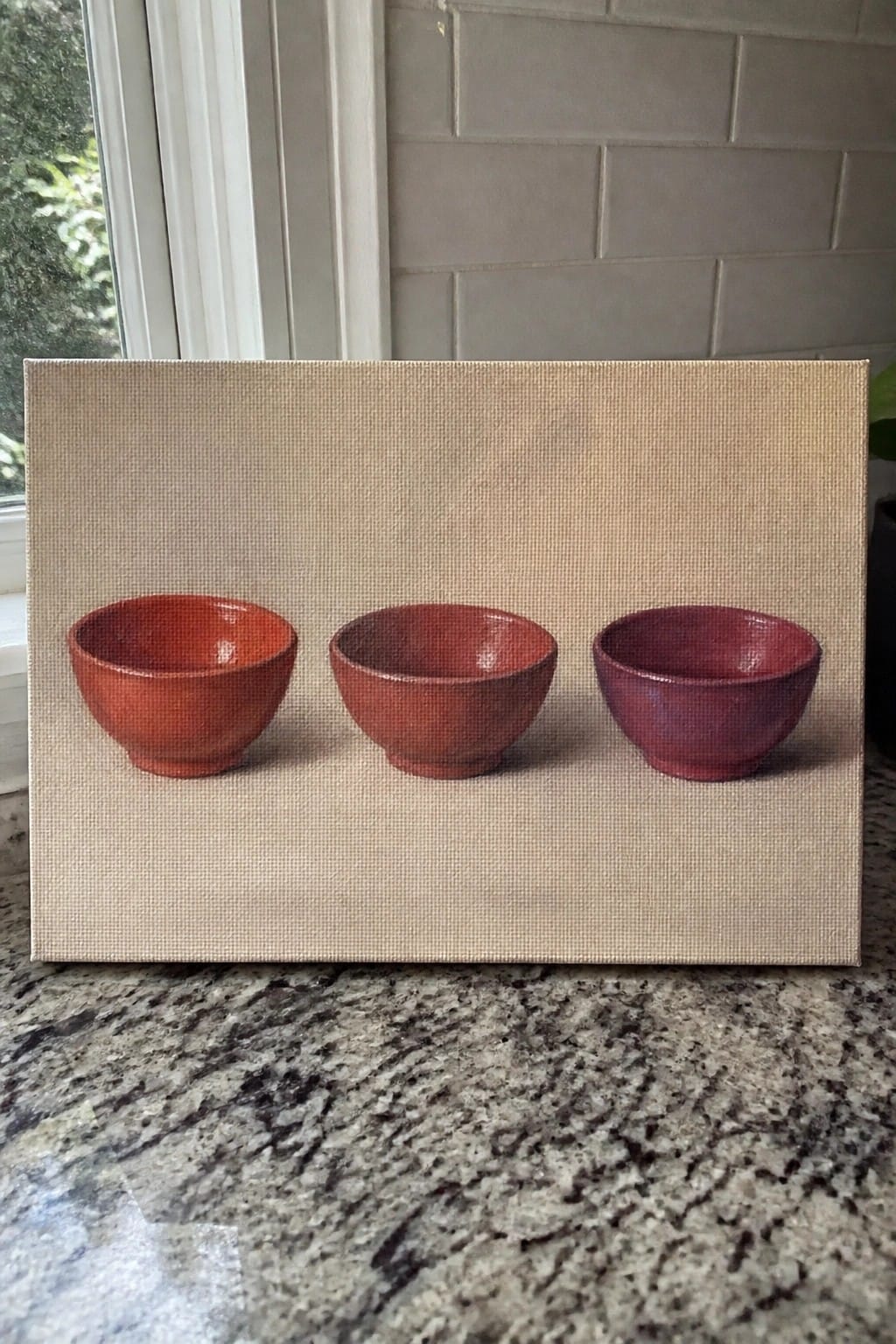 Three red ceramic bowls lined up on a beige canvas over granite.