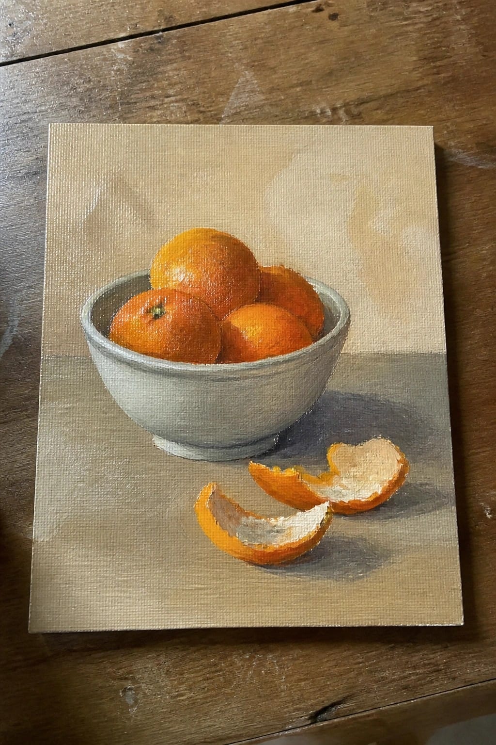 Still-life painting of oranges in a gray bowl with peels on a table.