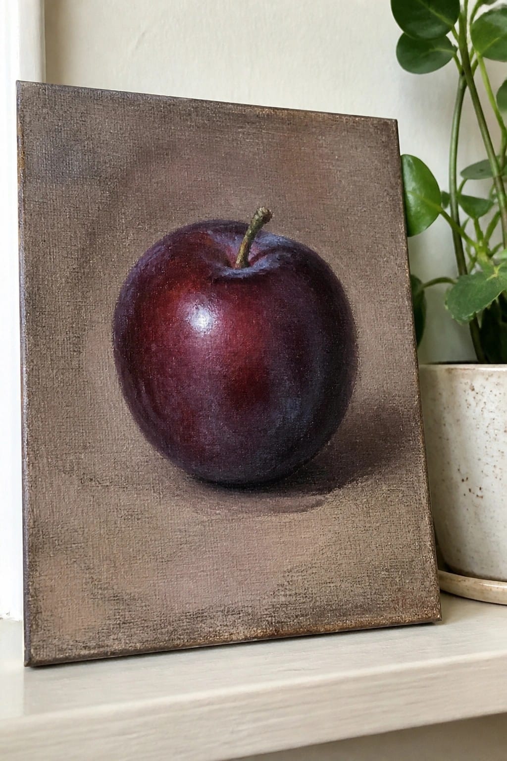 Realistic painting of glossy dark red apple on textured brown canvas beside plant.