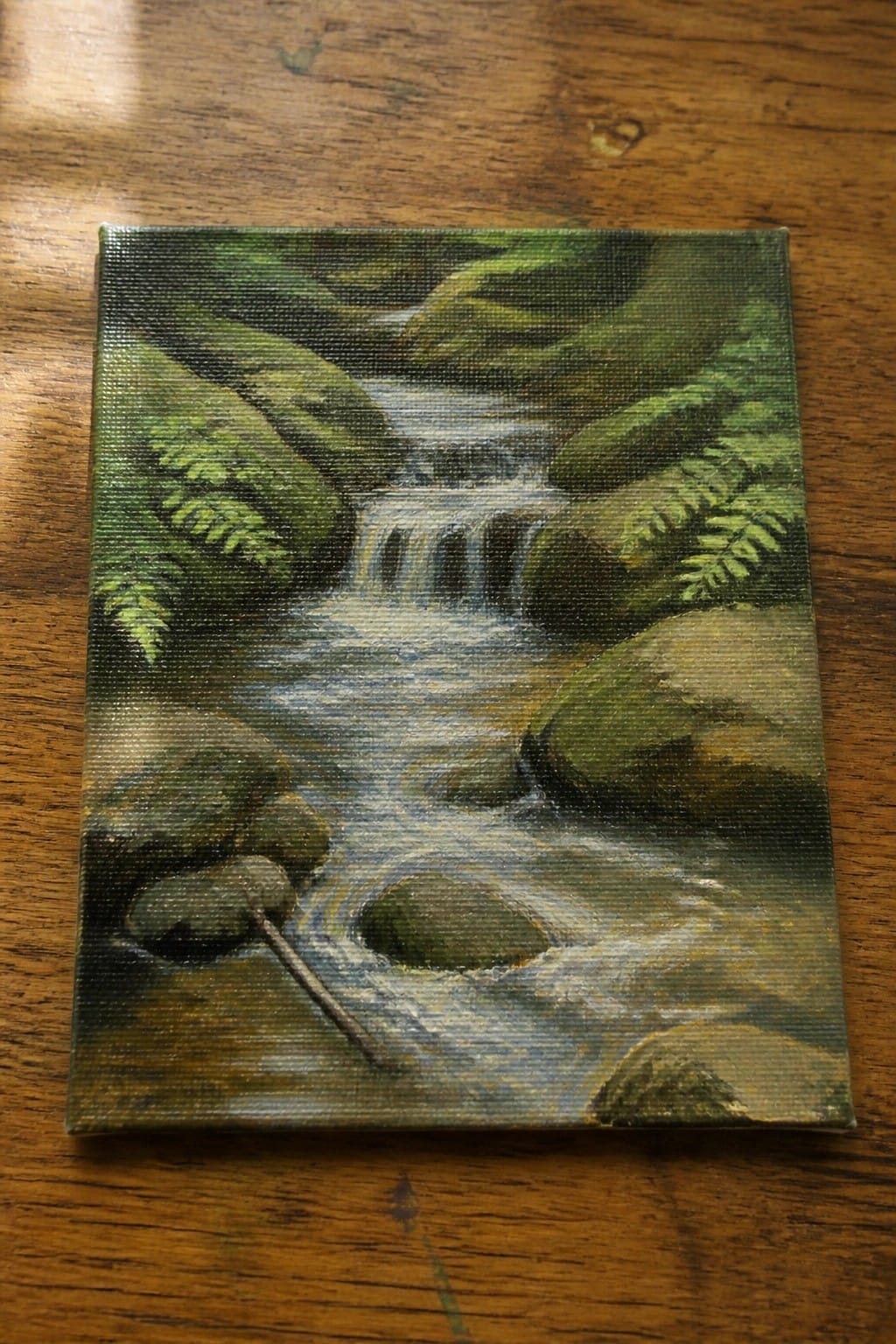 Painting of forest stream with waterfall, mossy rocks and green ferns on wood