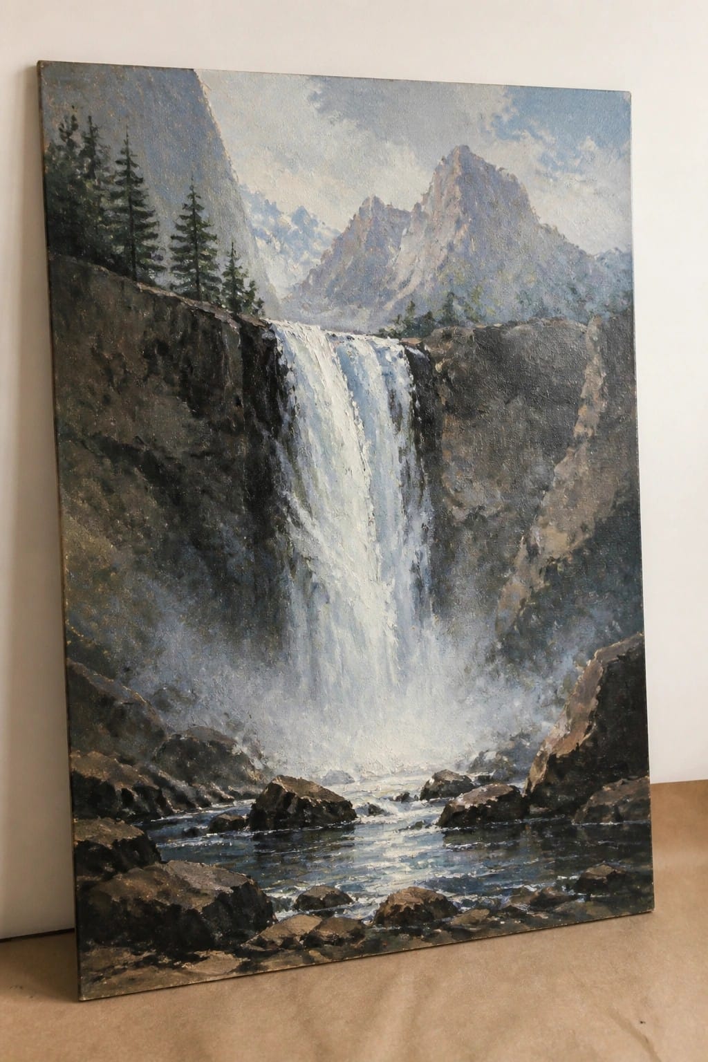 Cascading waterfall plunges down steep rocky cliffs into boulder-filled river with pine trees.