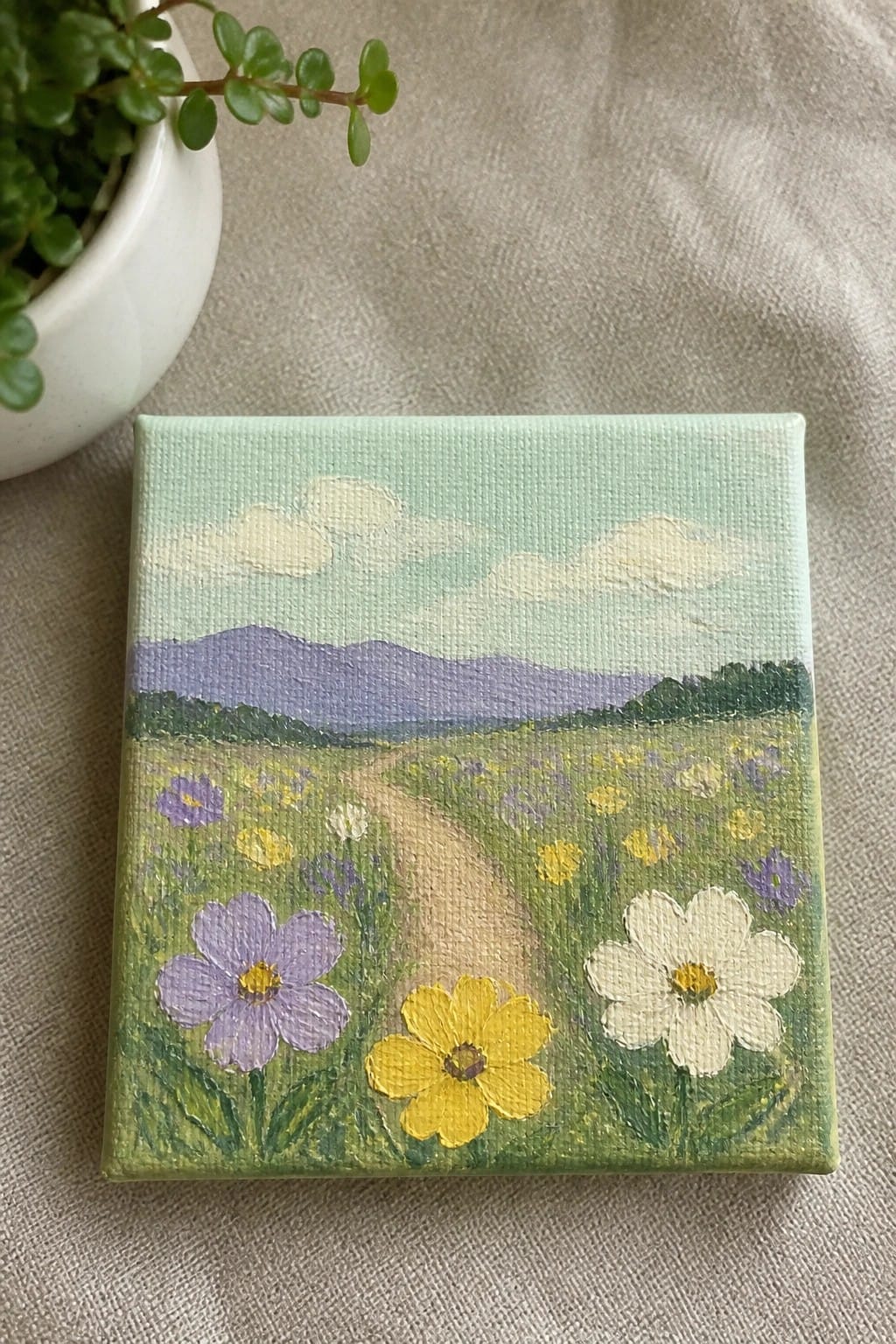 Small canvas painting of meadow path with purple mountains and wildflowers