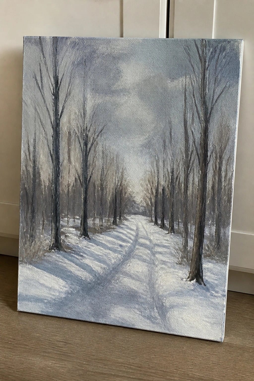 Painting of snowy path through leafless trees under overcast winter sky on canvas.