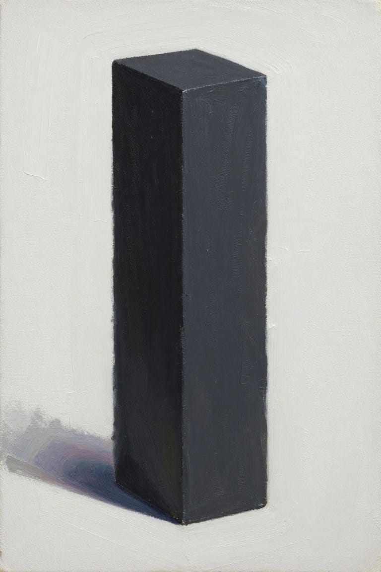 A tall dark rectangular block standing upright on a white surface with a soft shadow cast to the left against a plain light background.