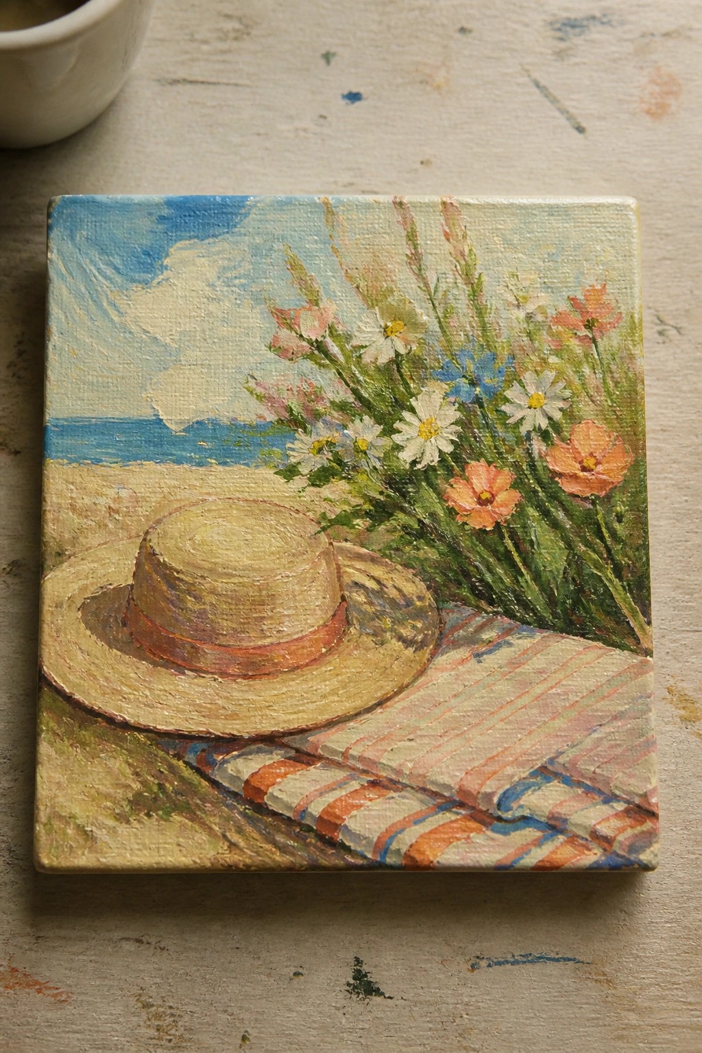 Straw hat on striped towel with wildflowers overlooking blue ocean and sky