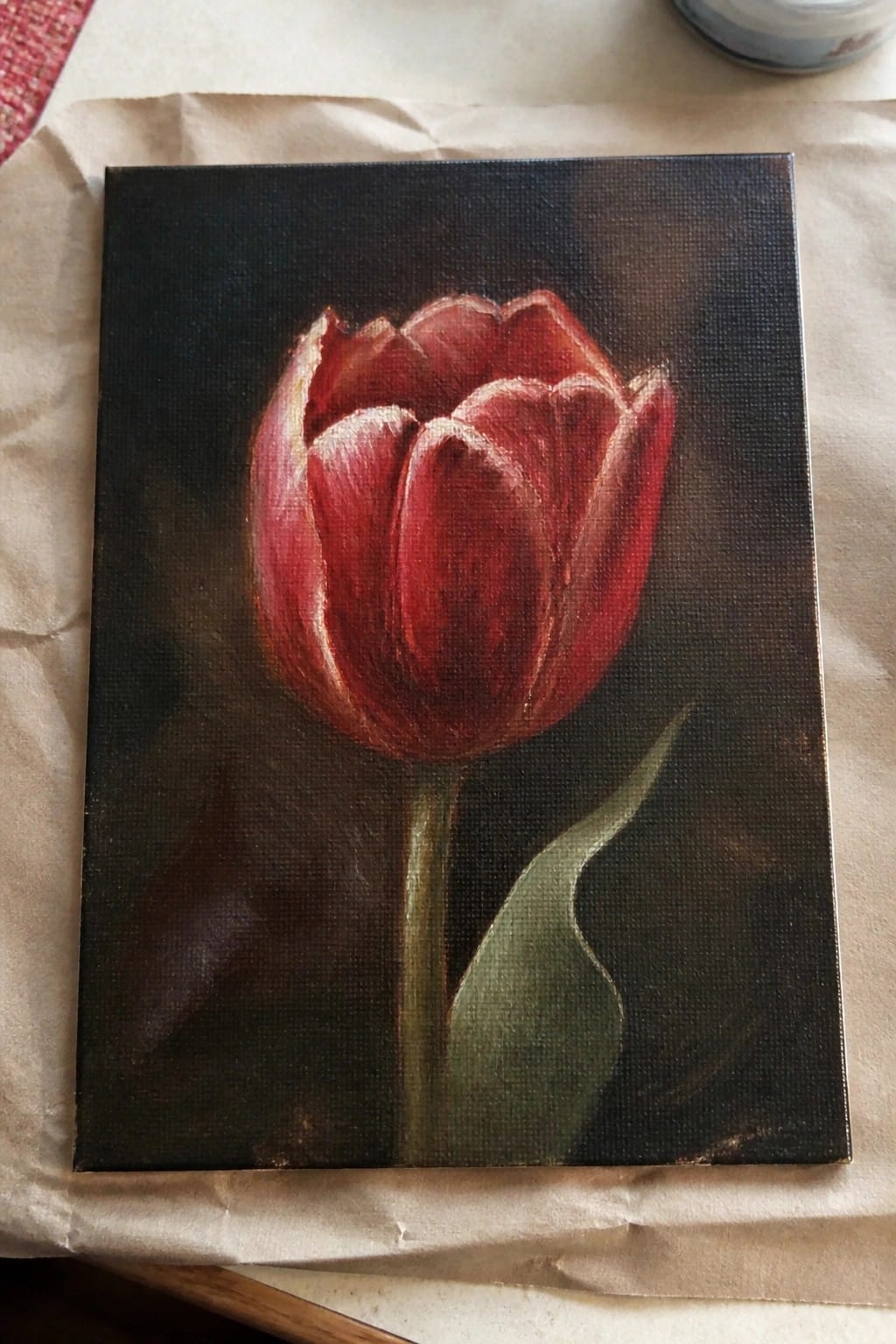 Realistic painting of a red tulip with green stem and leaf on dark background.