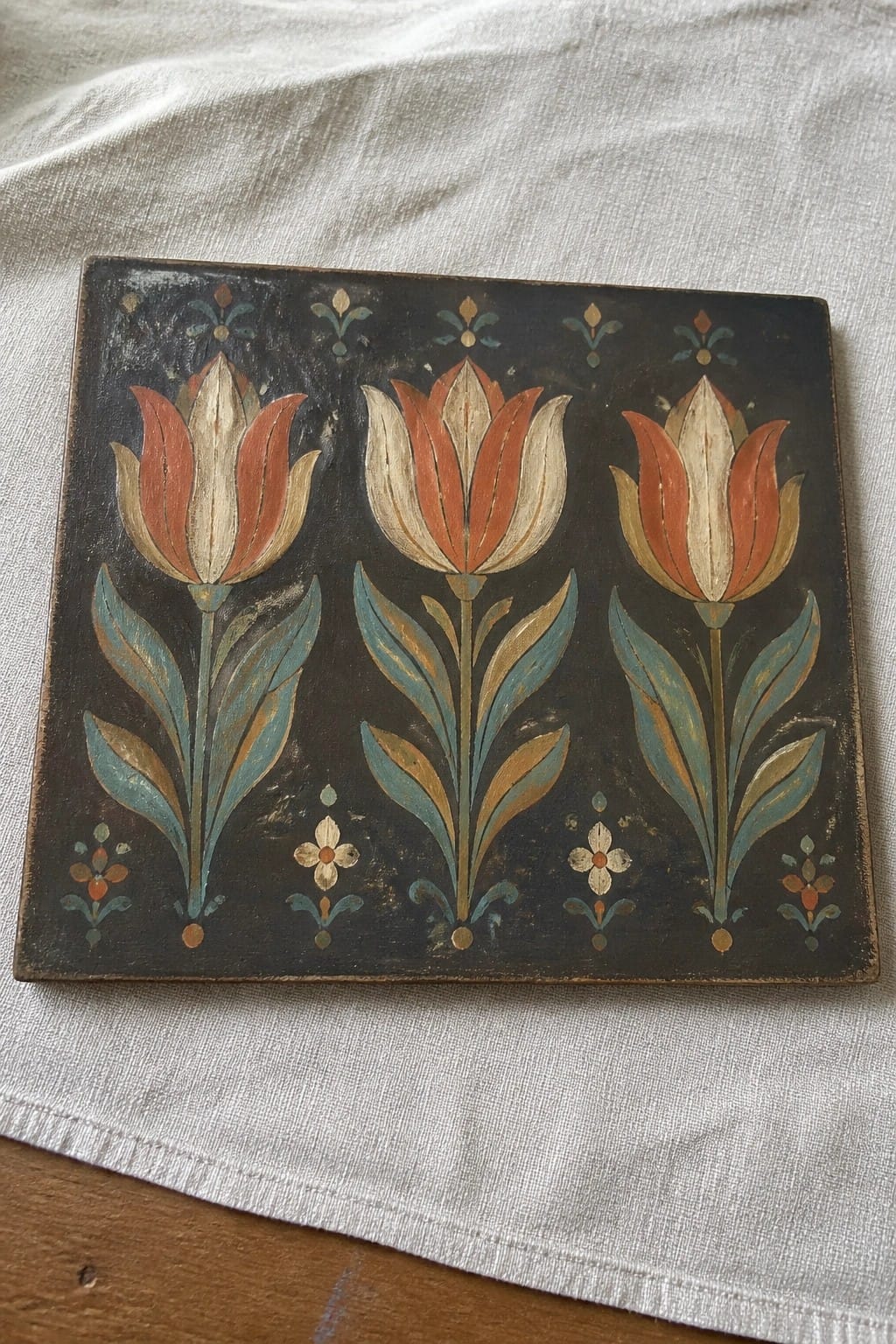 Three orange-white tulips with blue leaves painted on dark wooden panel