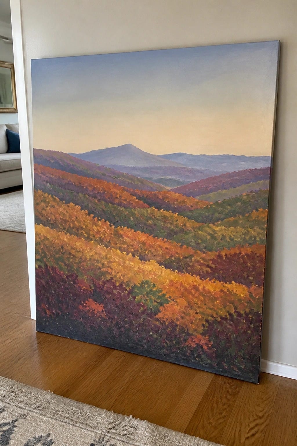Large autumn landscape painting of colorful hills leaning against wall on wood floor