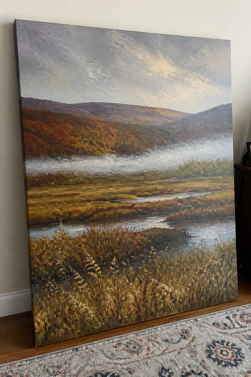 Large painting of misty autumn river valley leaning on wall above patterned rug