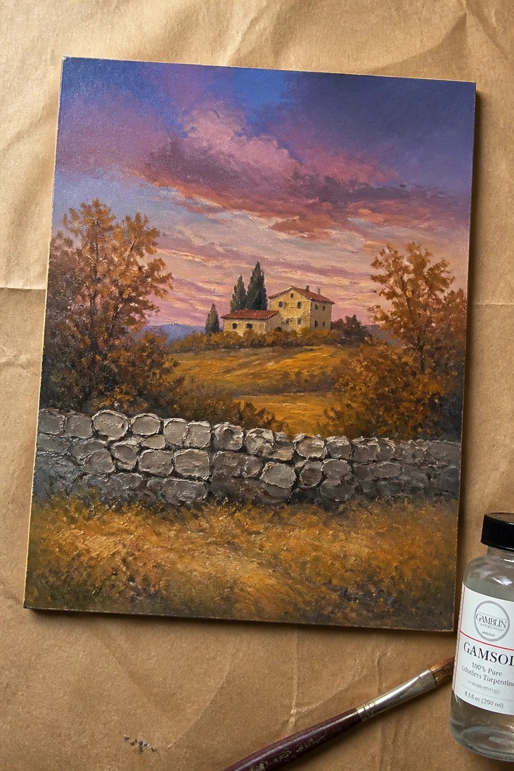 Oil painting of rural house behind stone wall under pink-purple sky beside Gamsol and brush