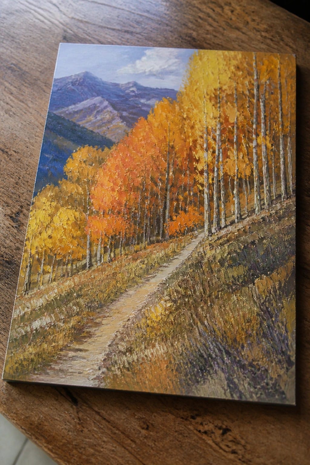 Impasto painting of winding path through vibrant orange and yellow autumn trees with mountains.