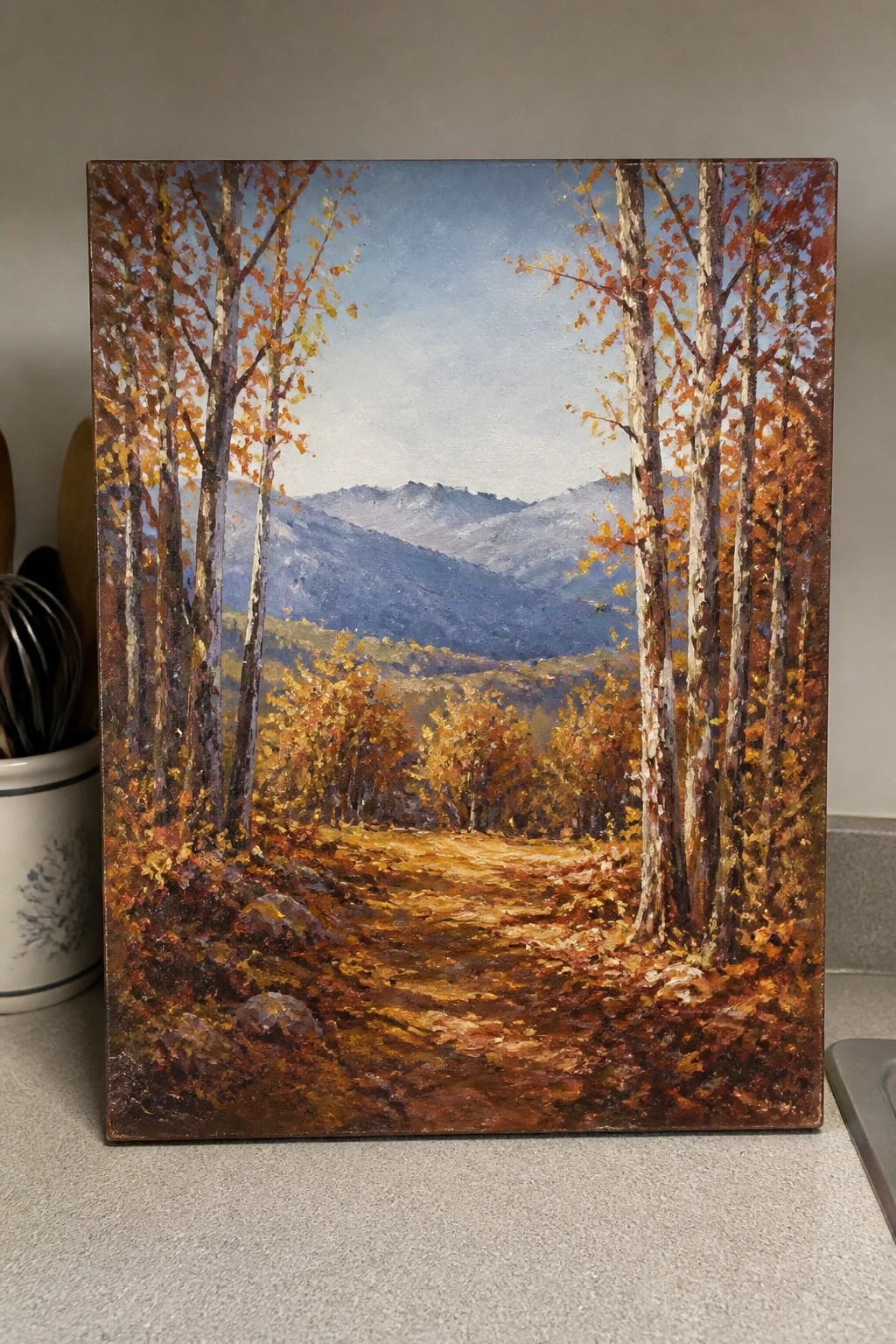 Autumn path winds through vibrant fall trees toward misty blue mountains.
