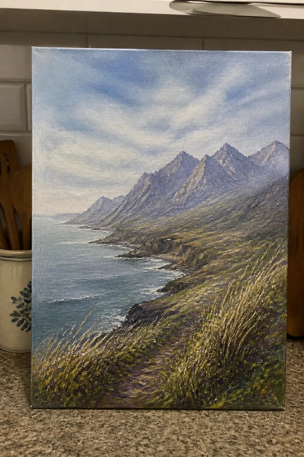 Landscape painting of grassy cliffs with path overlooking blue ocean and jagged mountains.