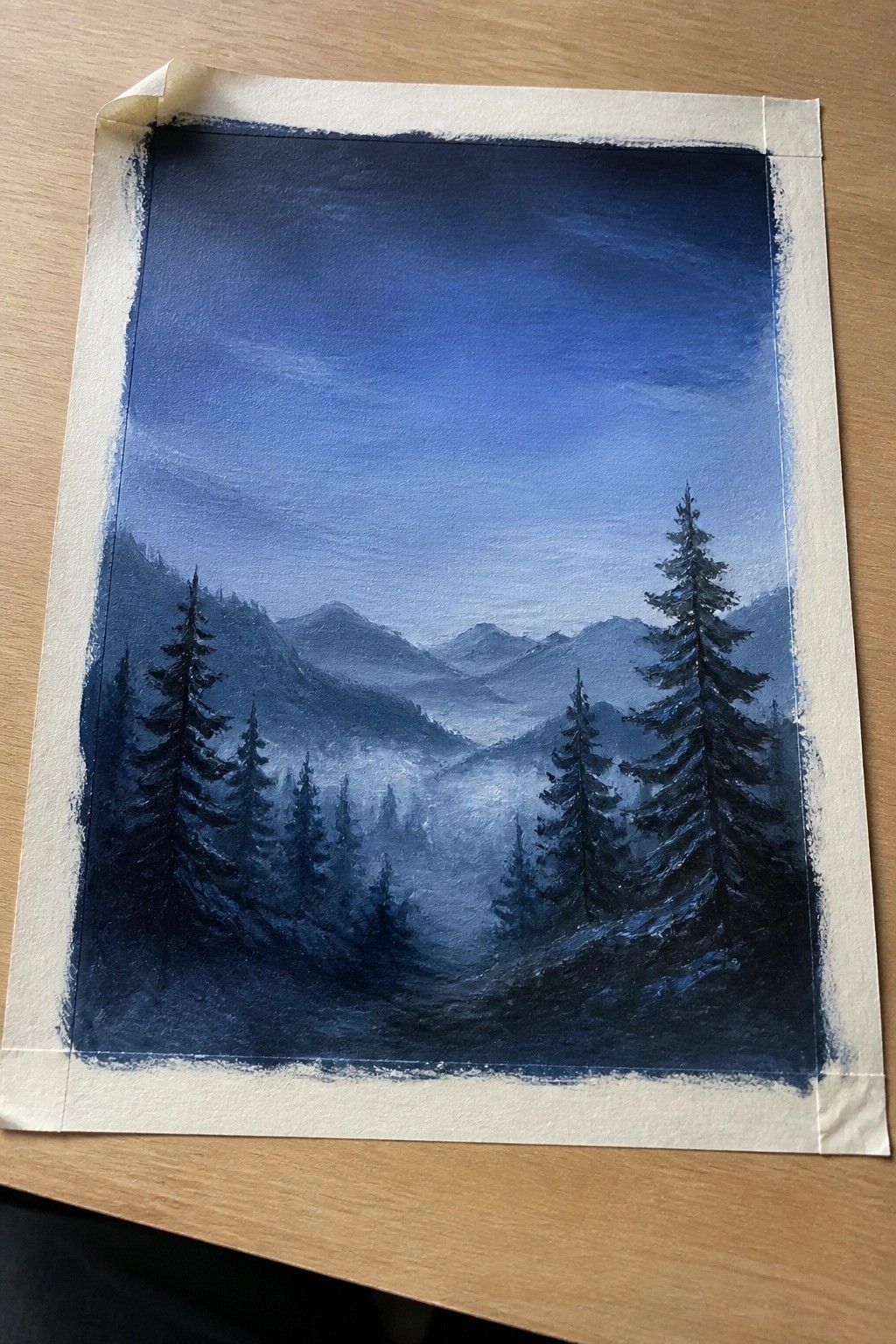 Blue-hued misty mountain landscape painting with pine trees taped on wood