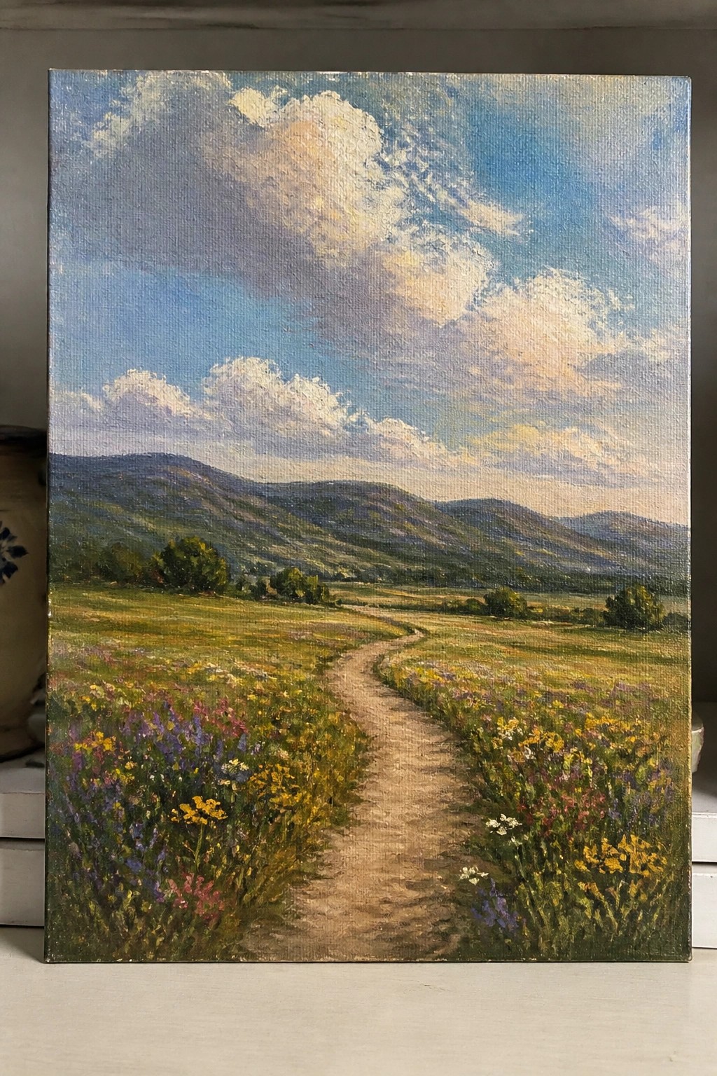 Dirt path winding through colorful wildflower meadow toward green hills under cloudy blue sky