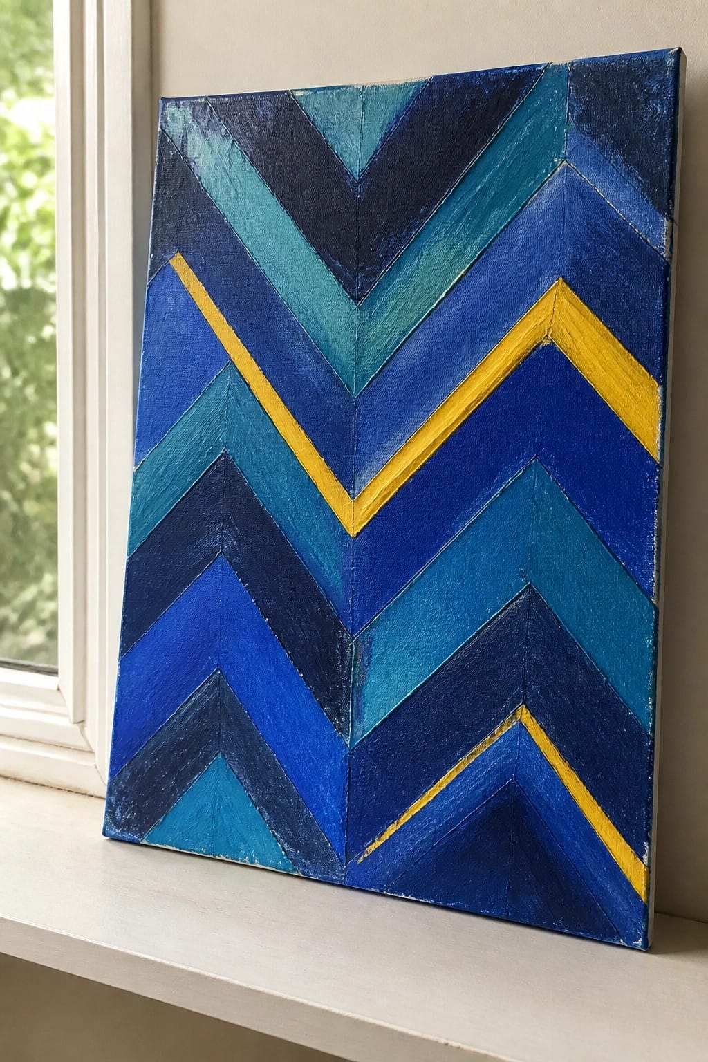 Abstract geometric painting with blue chevrons and yellow highlights on canvas by window