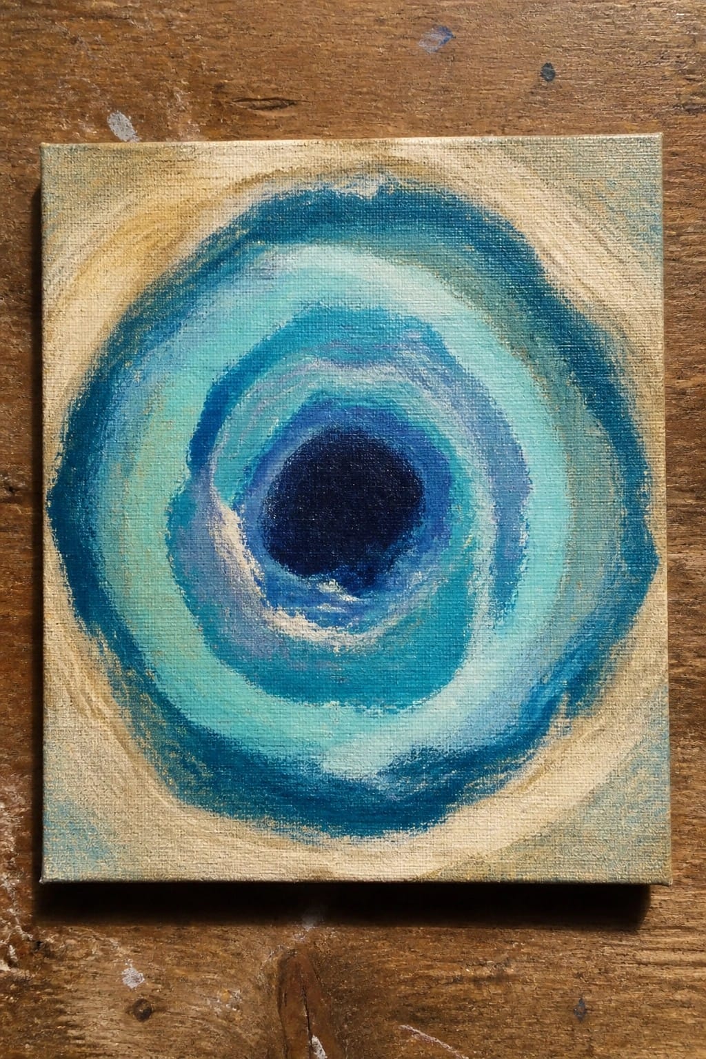 Abstract painting of concentric blue circles on square canvas atop wood.