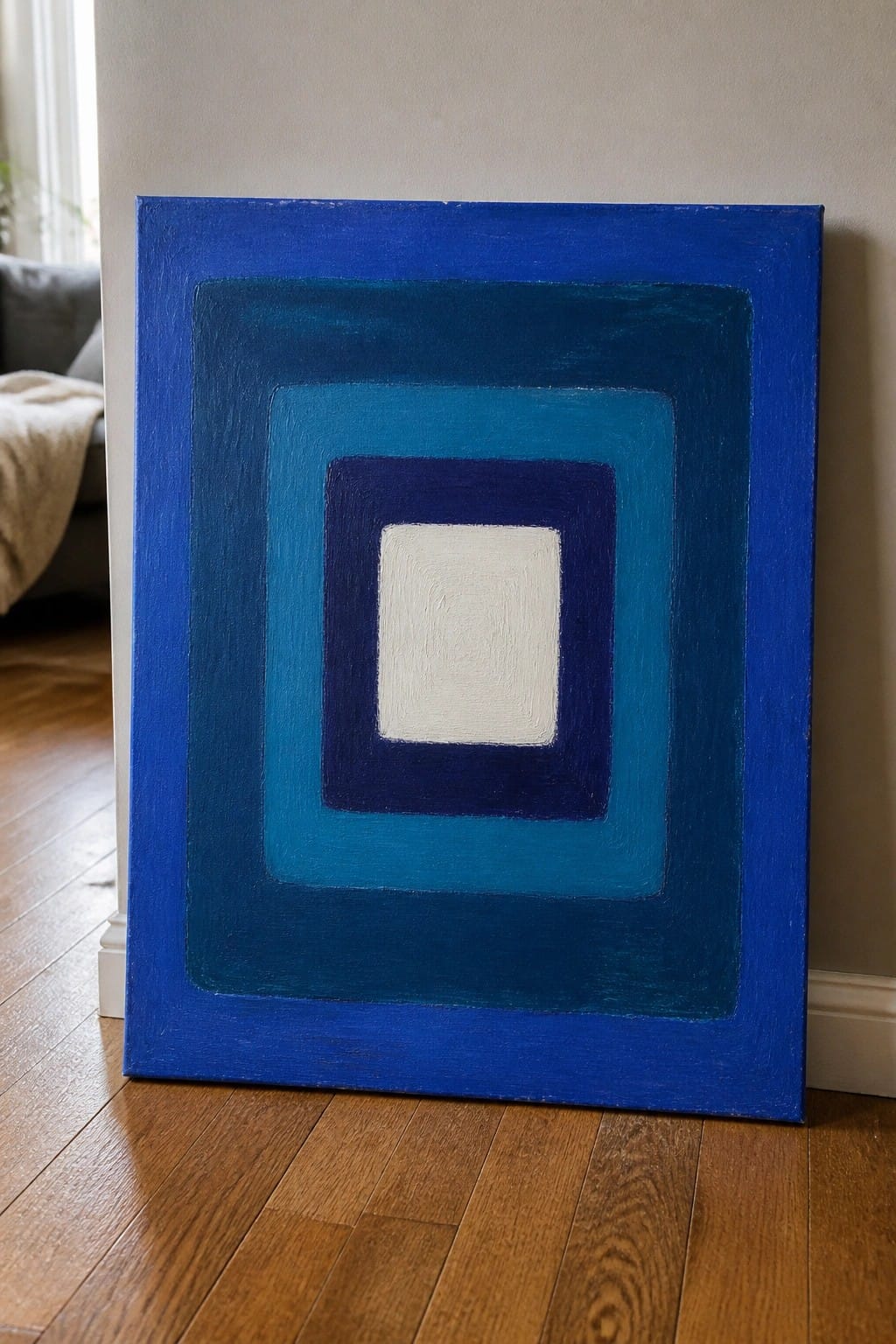 Abstract painting of concentric blue squares with white center on wooden floor