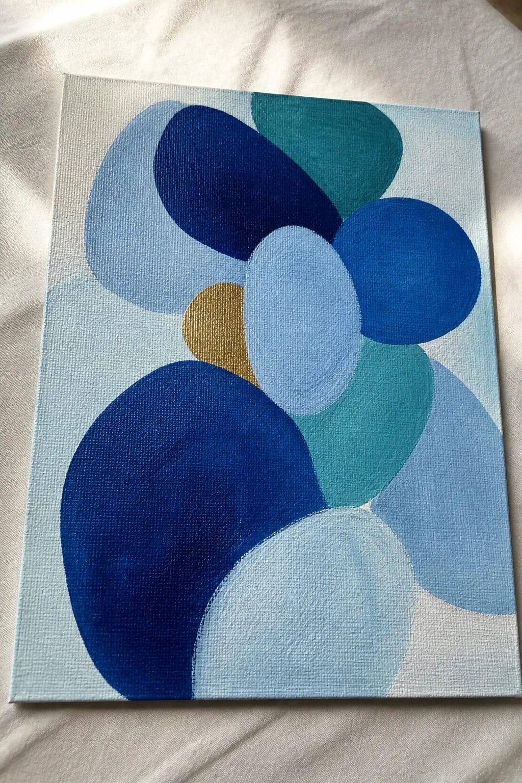 Abstract canvas painting with overlapping blue, teal, and gold circles on light blue background.