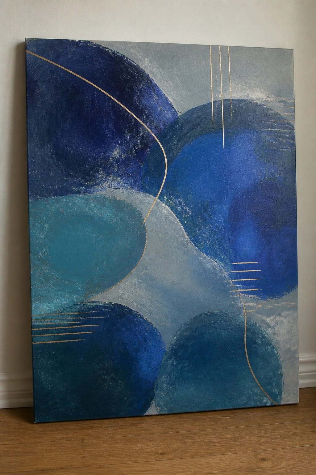 Abstract blue painting with overlapping circles and gold lines on canvas against wall