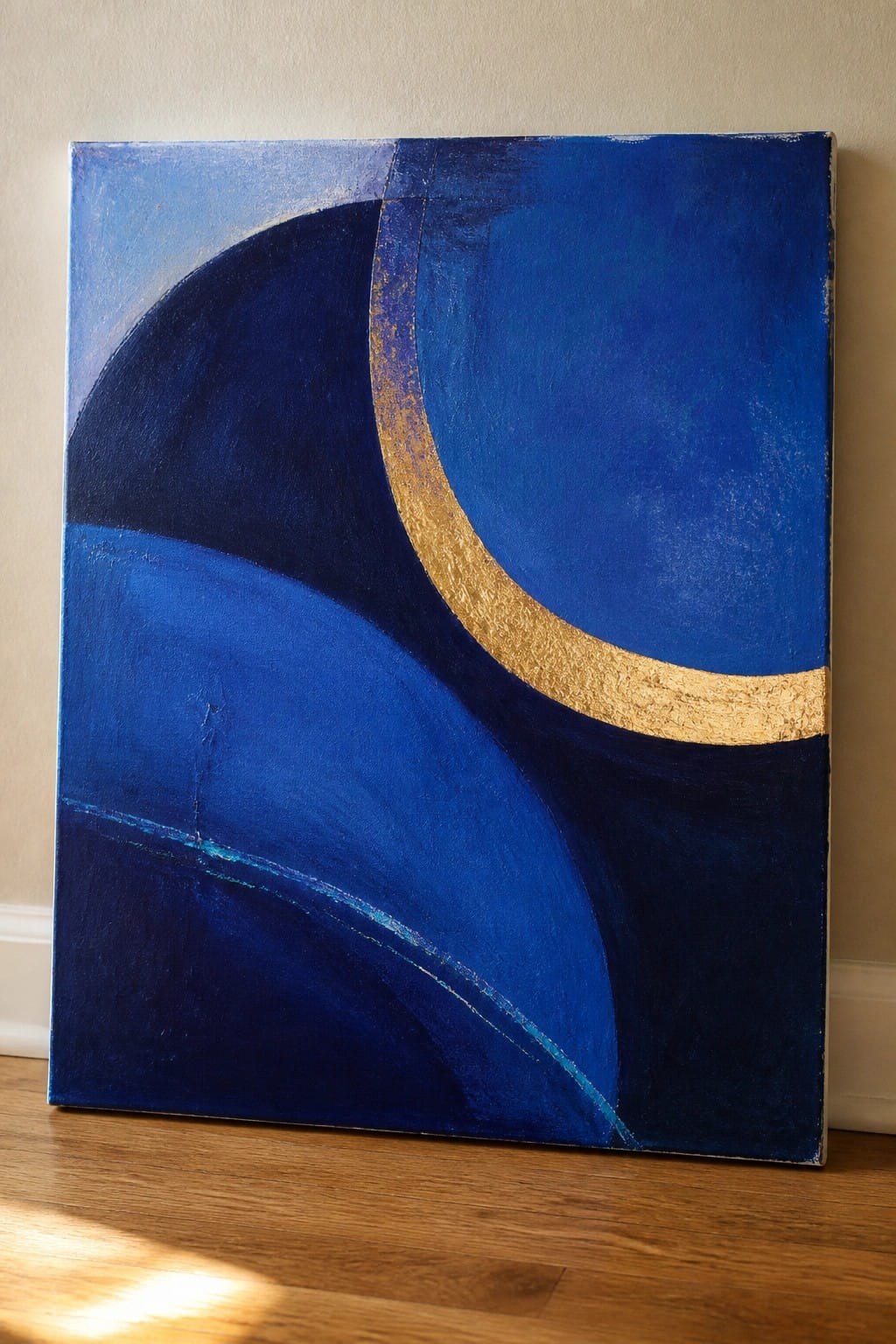 Abstract blue canvas with golden curved arc leaning on wooden floor against wall
