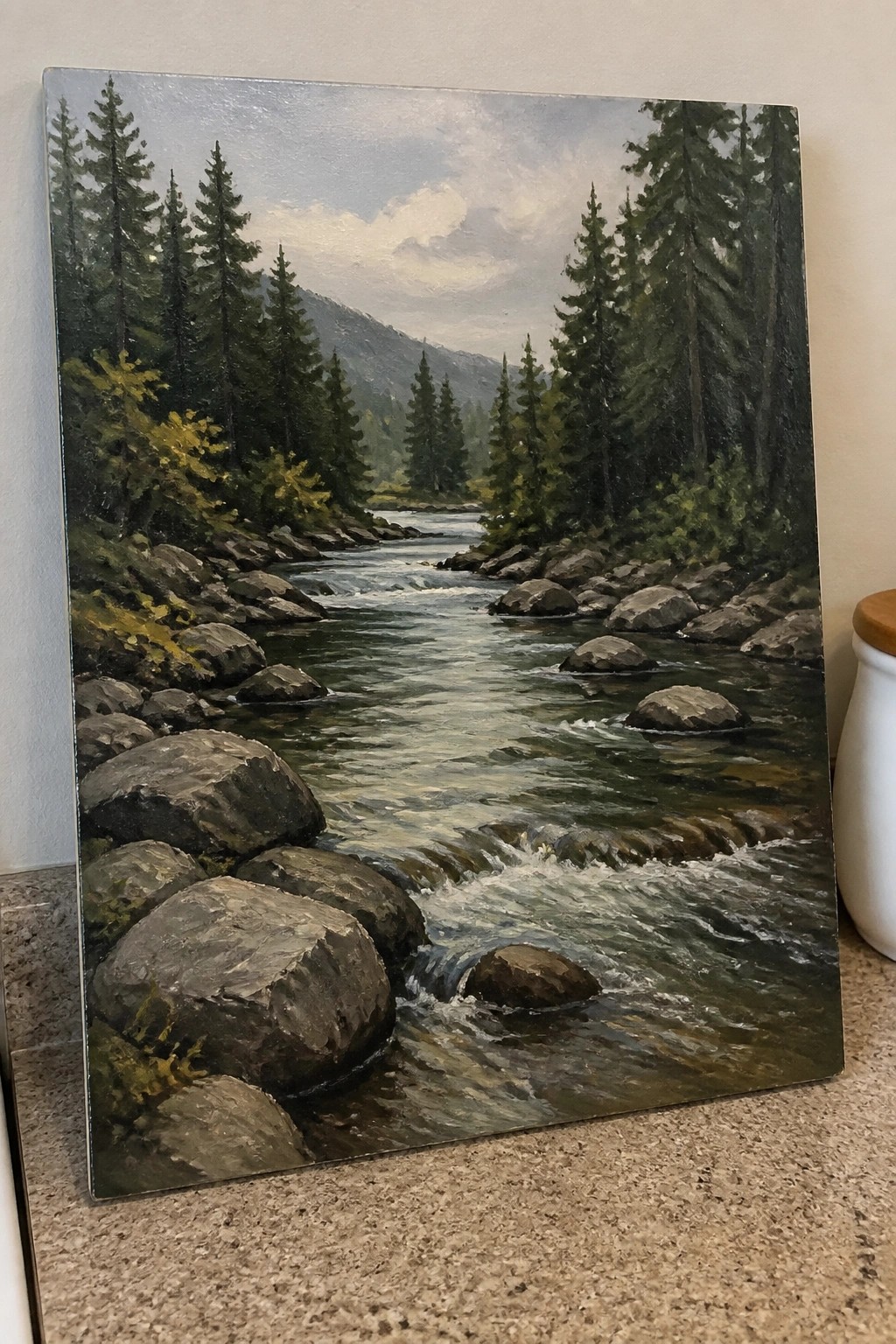 Realistic painting of a rocky river flowing through pine forest with mountains under clouds.