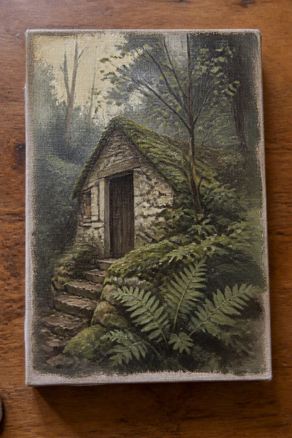 An oil painting of a moss-covered stone cottage in a misty forest with stone steps and ferns in the foreground.