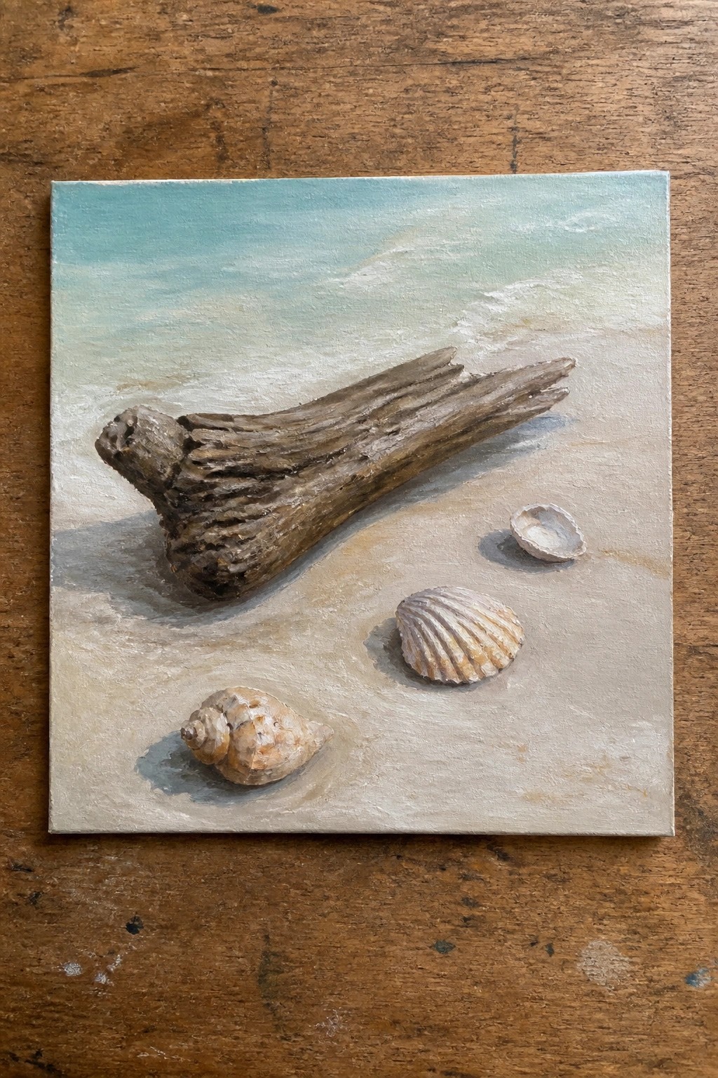Driftwood and seashells scattered on pale sand beside calm turquoise waves in a painting.
