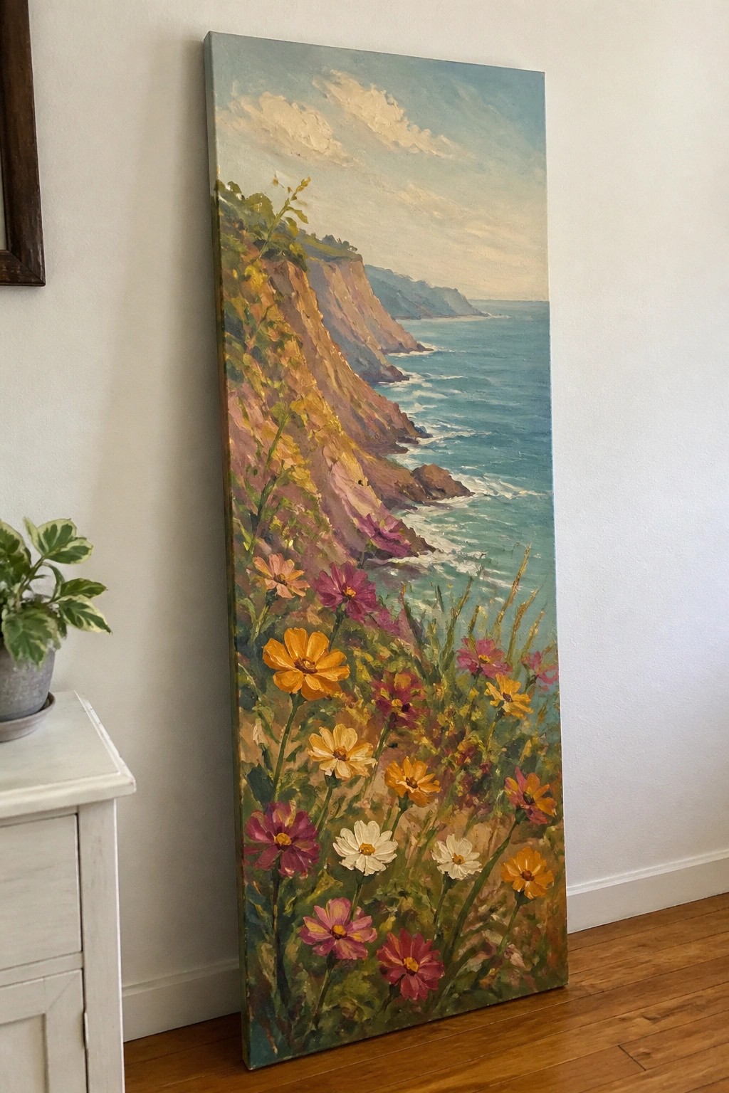 Large vertical painting of colorful wildflowers on cliffs above turquoise ocean.