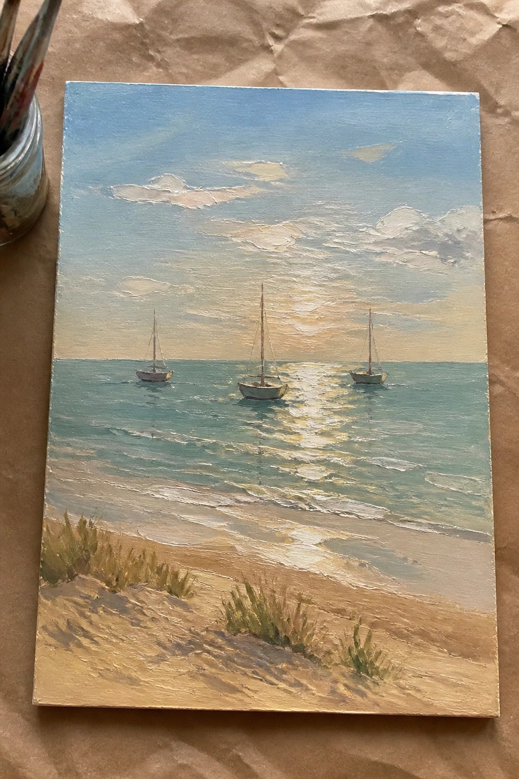 Three sailboats on calm sea at sunset above sandy beach with grass tufts