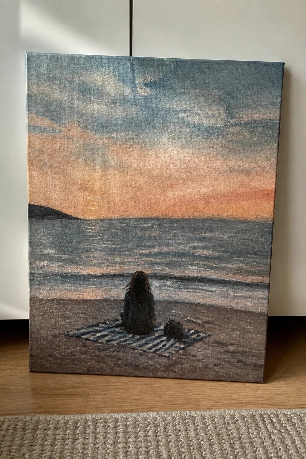 Woman sits on striped blanket with bag beside her on beach at sunset