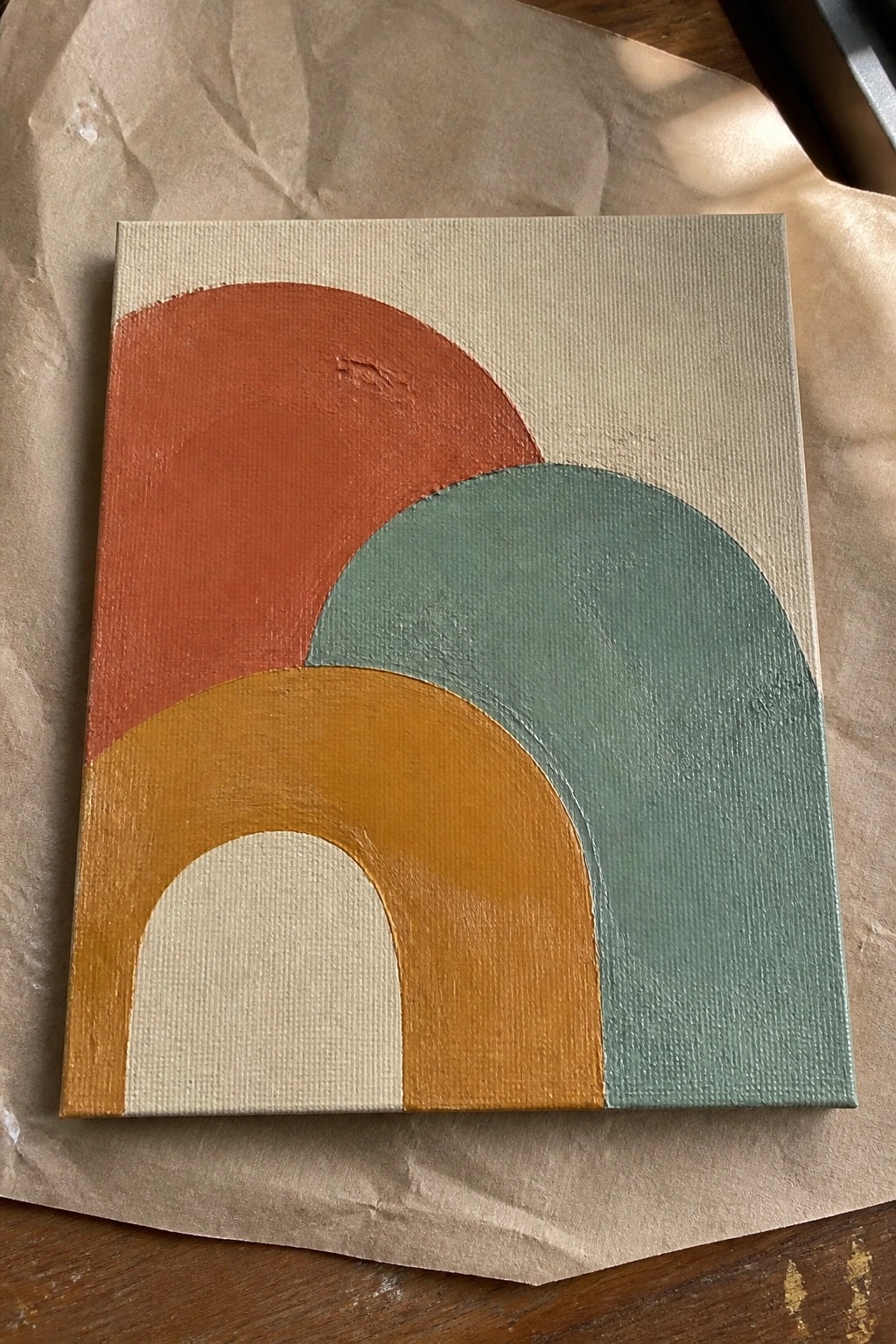Abstract painting with overlapping arches in orange, yellow, teal on beige canvas over brown paper.