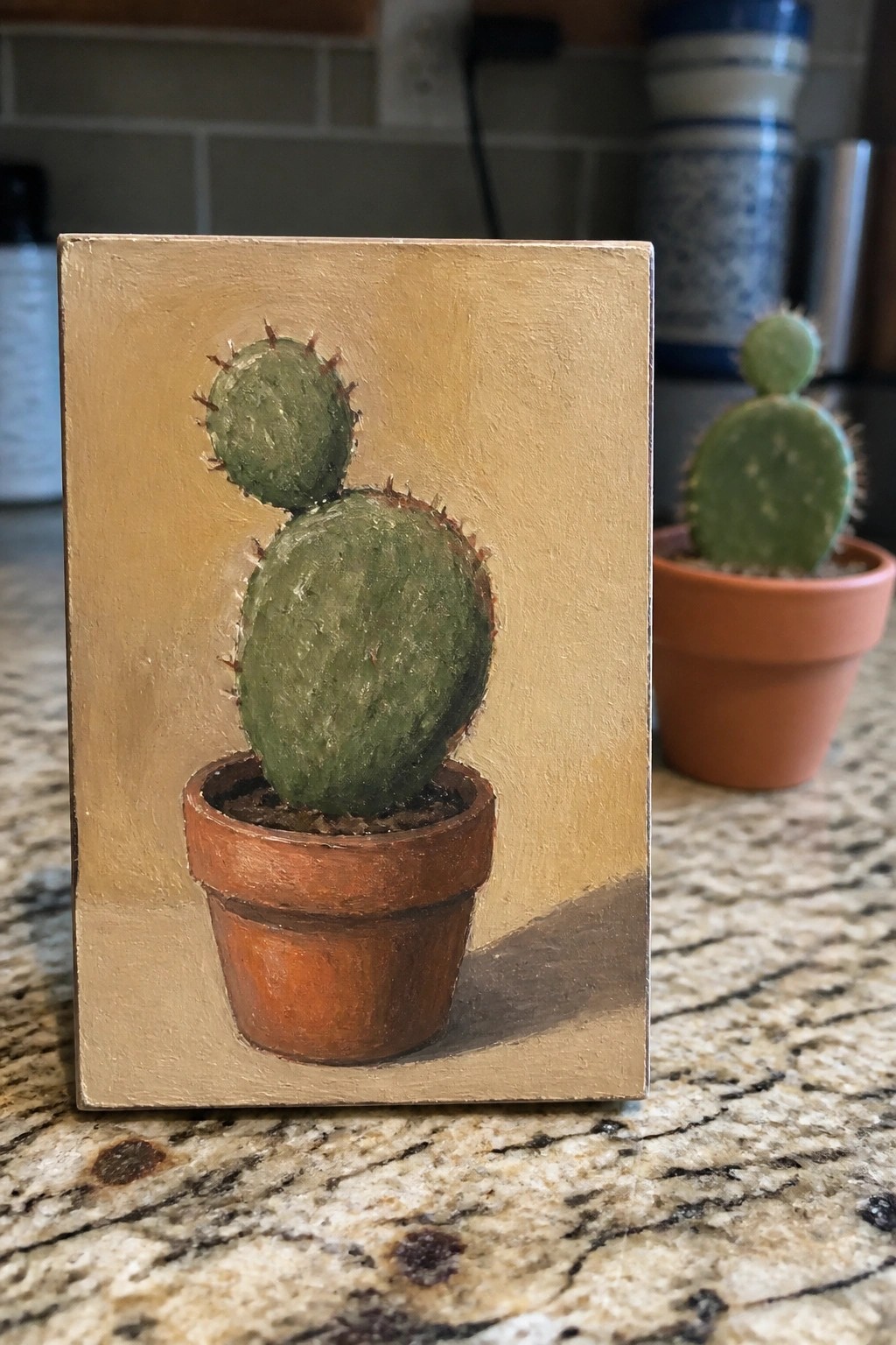 Painting of cactus in terracotta pot on marble counter with real plant nearby